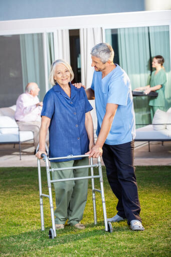 Portrait of senior woman being assisted by male caretaker in using Zimmer frame at nursing home lawn