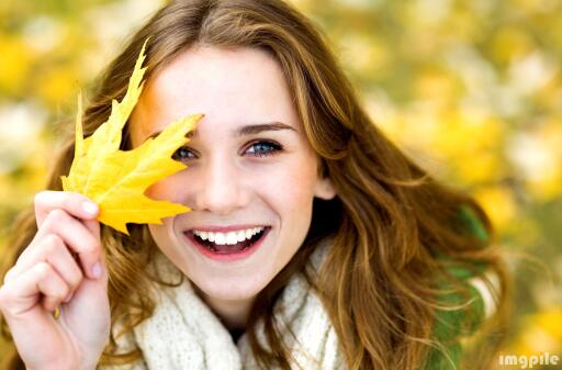 Beautiful girl smiling with maple leaves in autumn sunshine
